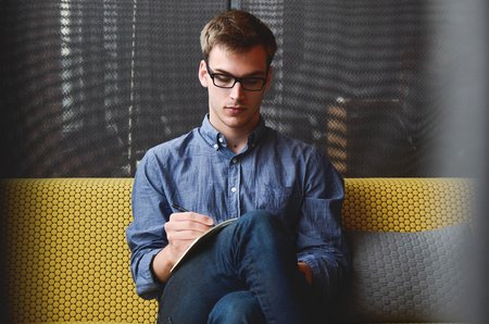 Hombre joven sentado en un sofá tomando notas, participando en pruebas de usuario para Volkswagen Financial Services