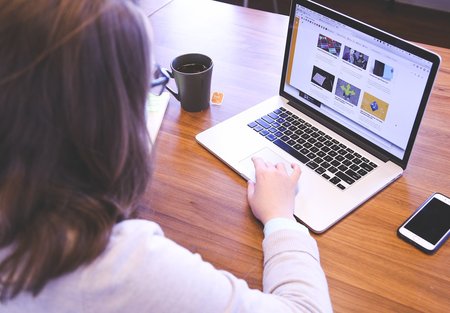 Mujer trabajando en un portátil con una taza de café al lado y un teléfono móvil sobre la mesa, participando en pruebas de usuario para Volkswagen Financial Services